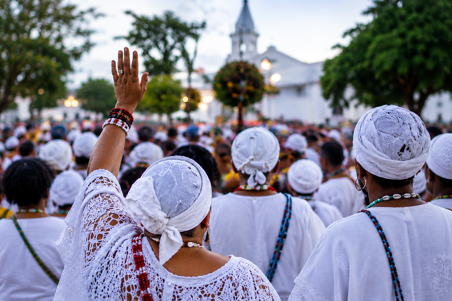 Povos de terreiro reunidos diante de uma igreja, com uma mulher erguendo a mão